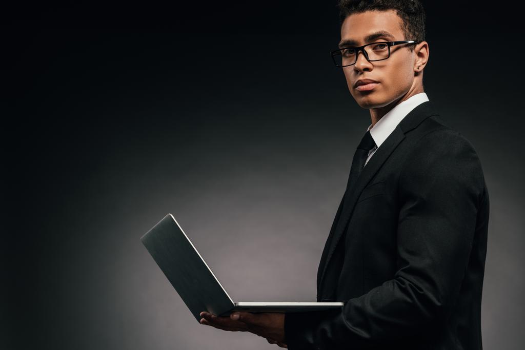 vue latérale de l'homme d'affaires afro-américain tenant un ordinateur portable sur fond sombre
 - Photo, image