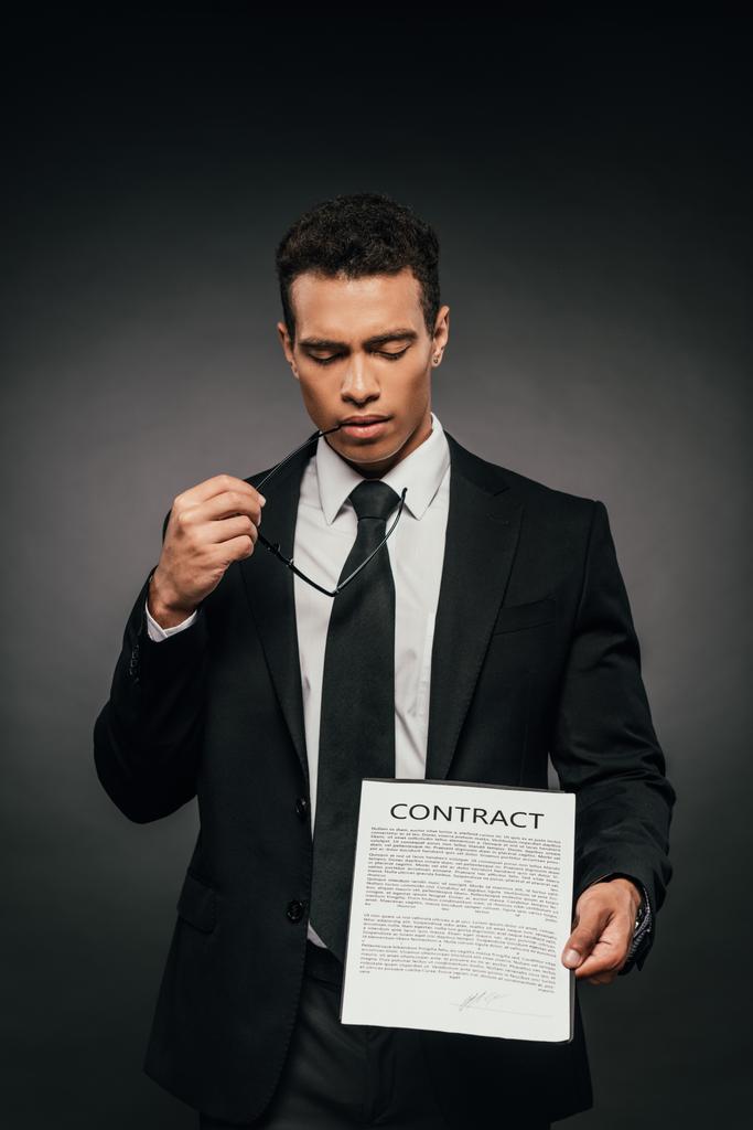 thoughtful african american businessman showing contract on dark background - Photo, Image