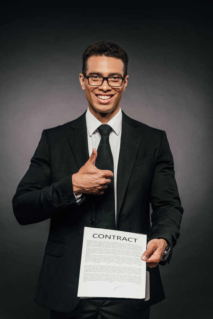 boldog afro-amerikai üzletember bemutatás szerződés és hüvelykujj megjelöl-ra sötét háttér - Fotó, kép