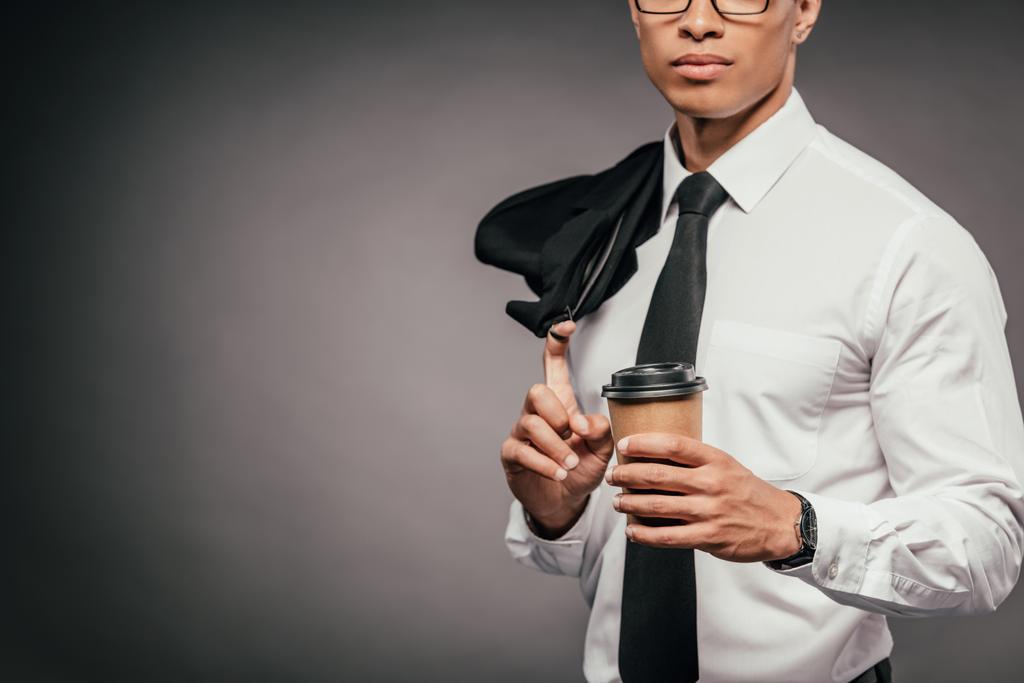 cropped view of african american businessman holding blazer and coffee to go on dark background - Photo, Image