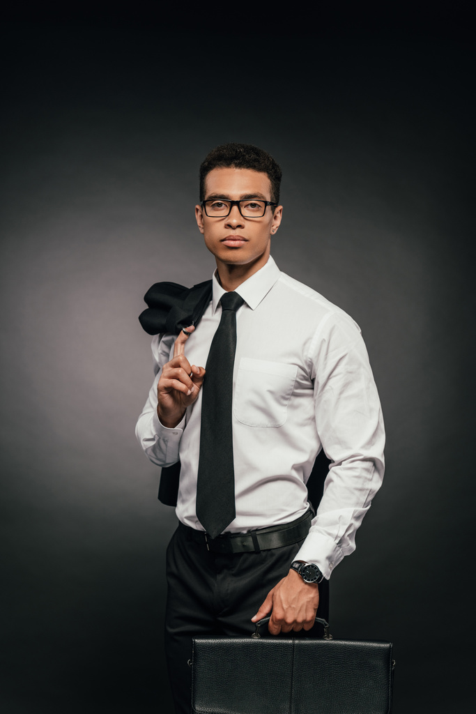 Afrikanisch-amerikanischer Geschäftsmann mit Blazer und Lederaktentasche auf dunklem Hintergrund - Foto, Bild