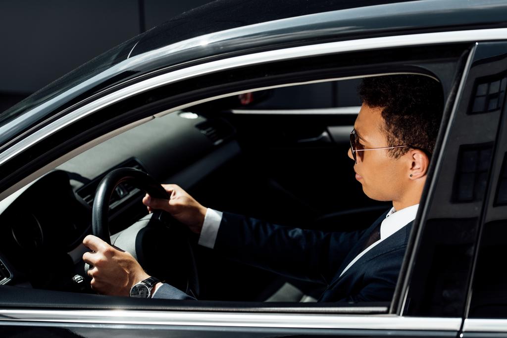 puolella näkymä afrikkalainen amerikkalainen liikemies puku ja aurinkolasit ajo auto aurinkoisena päivänä
 - Valokuva, kuva