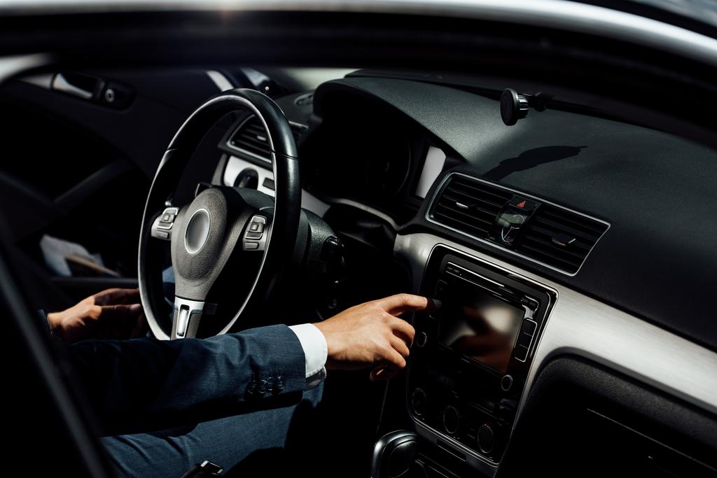 Ausgeschnittene Ansicht eines afrikanisch-amerikanischen Geschäftsmannes im Anzug, der im Auto Knopf drückt - Foto, Bild
