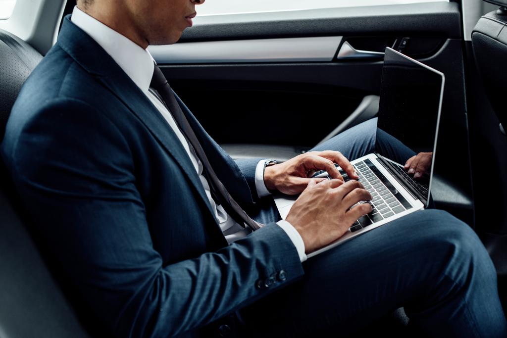 Ausgeschnittene Ansicht eines afrikanisch-amerikanischen Geschäftsmannes mit Laptop im Auto - Foto, Bild