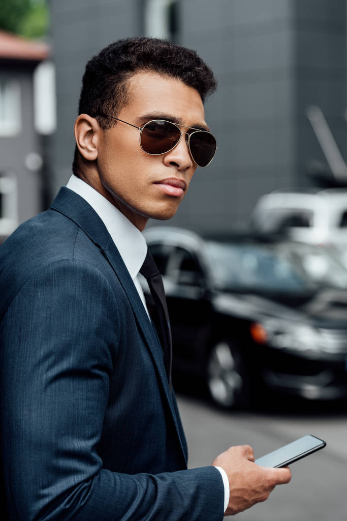 beau et confiant homme d'affaires afro-américain en costume et lunettes de soleil en utilisant smartphone
 - Photo, image