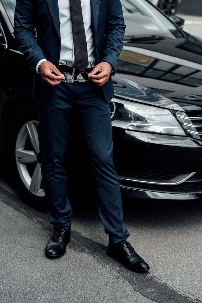cropped view of african american man in suit holding sunglasses near car - Photo, Image