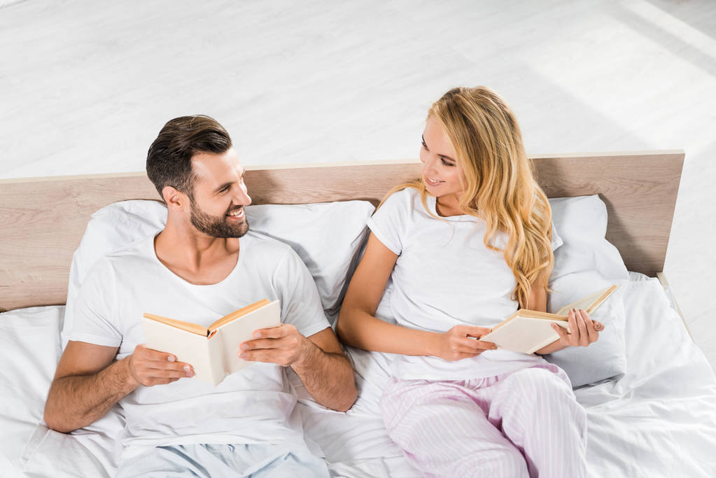 hermosa pareja sonriente acostada en la cama con libros en casa
  - Foto, imagen