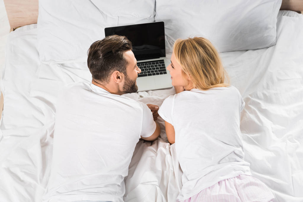 Vista posteriore della coppia sdraiata a letto e utilizzando il computer portatile a casa
  - Foto, immagini