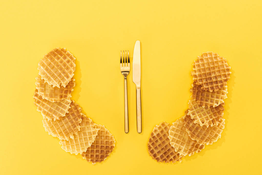 vista superior de waffles crocantes e deliciosos com talheres no meio isolado no amarelo
 - Foto, Imagem