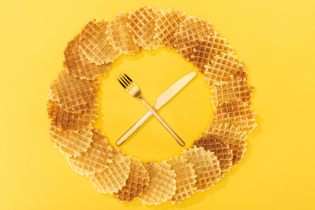 Top uitzicht van wafels in cirkel met vork en mes in het midden op geel - Foto, afbeelding