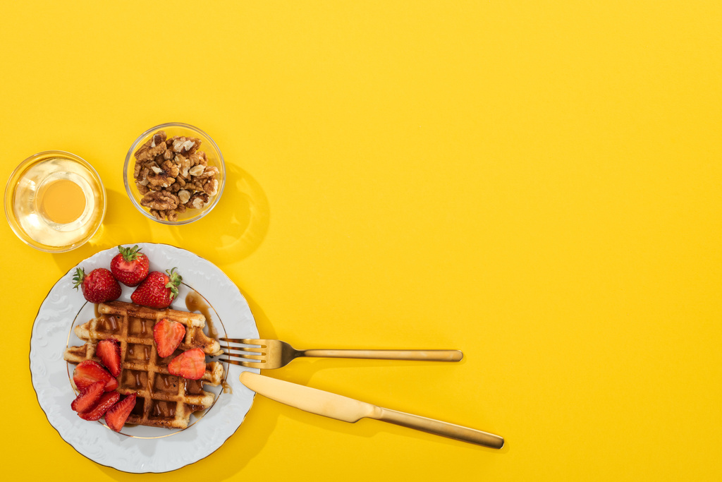 top view of waffles, berries, honey and nuts near cutlery on yellow - Photo, Image