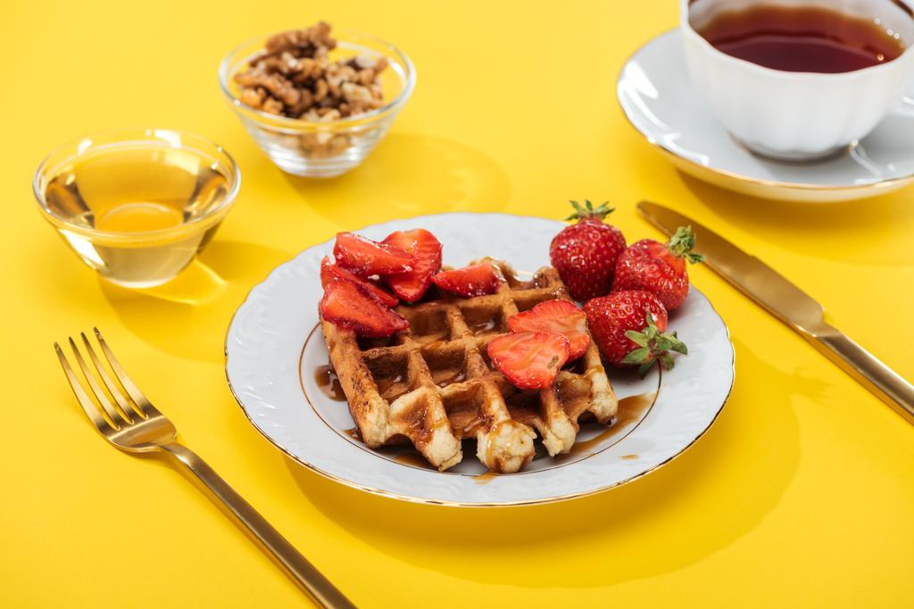 servi le petit déjeuner avec gaufres, fraises, miel, noix et thé sur jaune
 - Photo, image