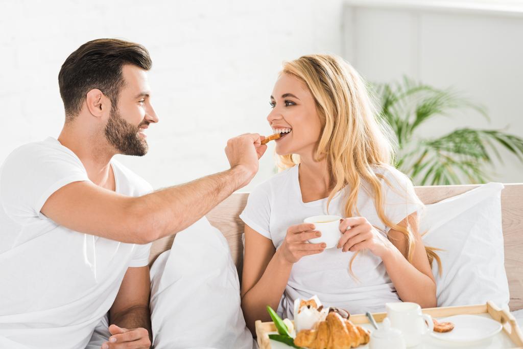 beautiful couple in pajamas having breakfast in bed in morning - Photo, Image