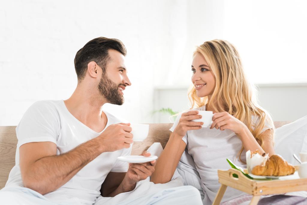 beautiful couple with cups during breakfast in bed in morning - Photo, Image