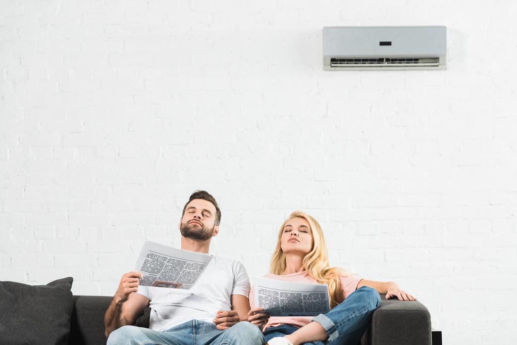 Paar auf Couch mit Zeitungen, die zu Hause unter Hitze leiden - Foto, Bild