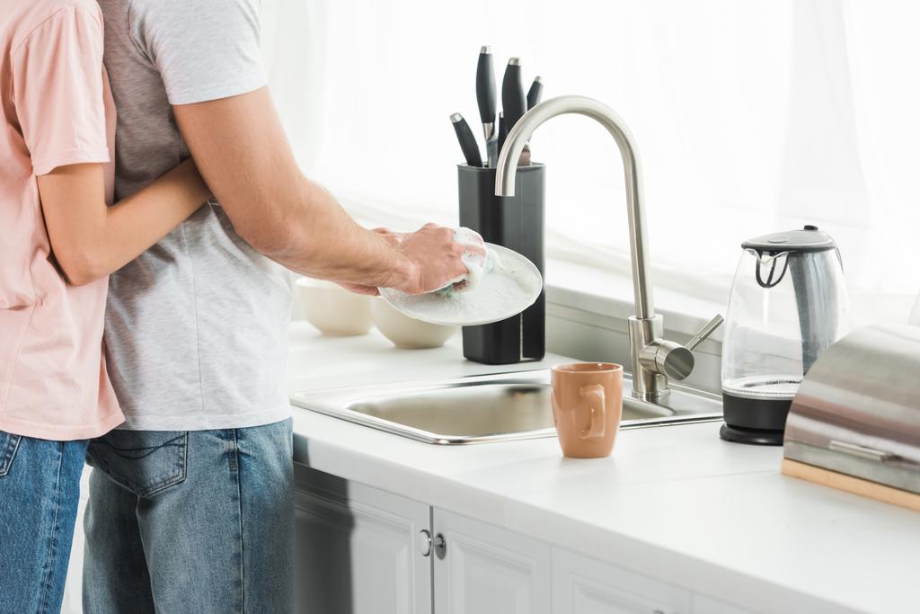Rajatut näkymä nainen halaus mies tiskaus keittiössä
 - Valokuva, kuva