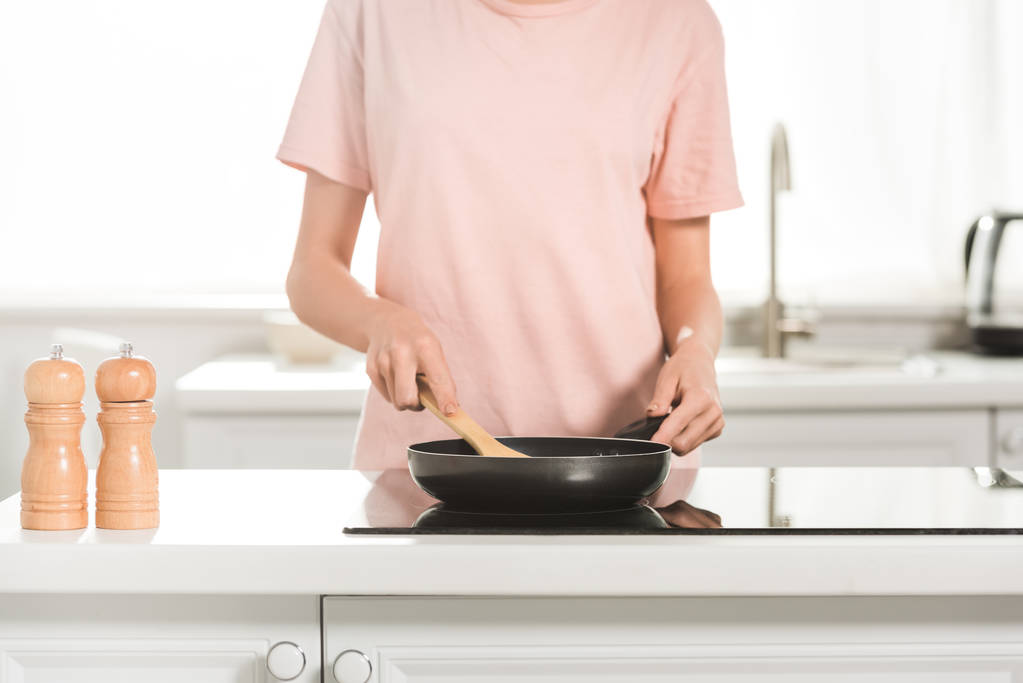rajattu näkymä nainen ruoanlaitto paistinpannu ja lastalla keittiössä aamulla
 - Valokuva, kuva