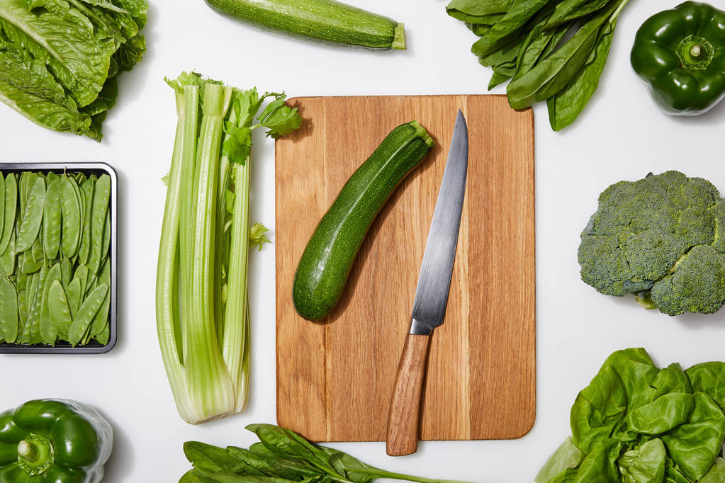top view of green vegetables and wooden chopping board with knife on white background - Photo, Image