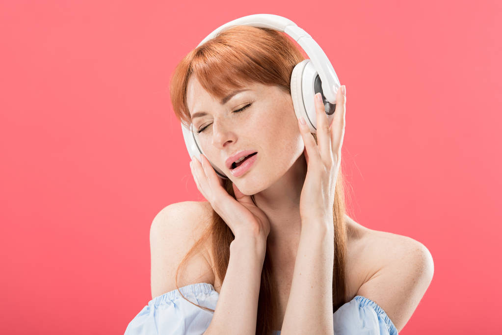jolie rousse femme écouter de la musique dans les écouteurs avec les yeux fermés isolé sur rose
 - Photo, image