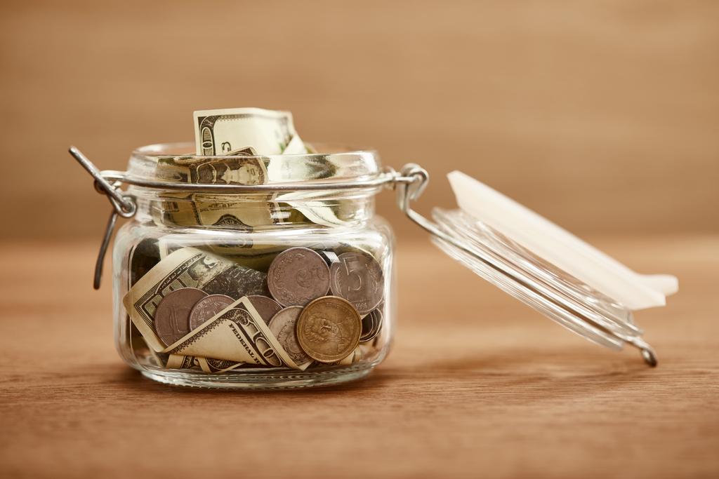 glazen pot met munten en dollar bankbiljetten op houten tafel - Foto, afbeelding