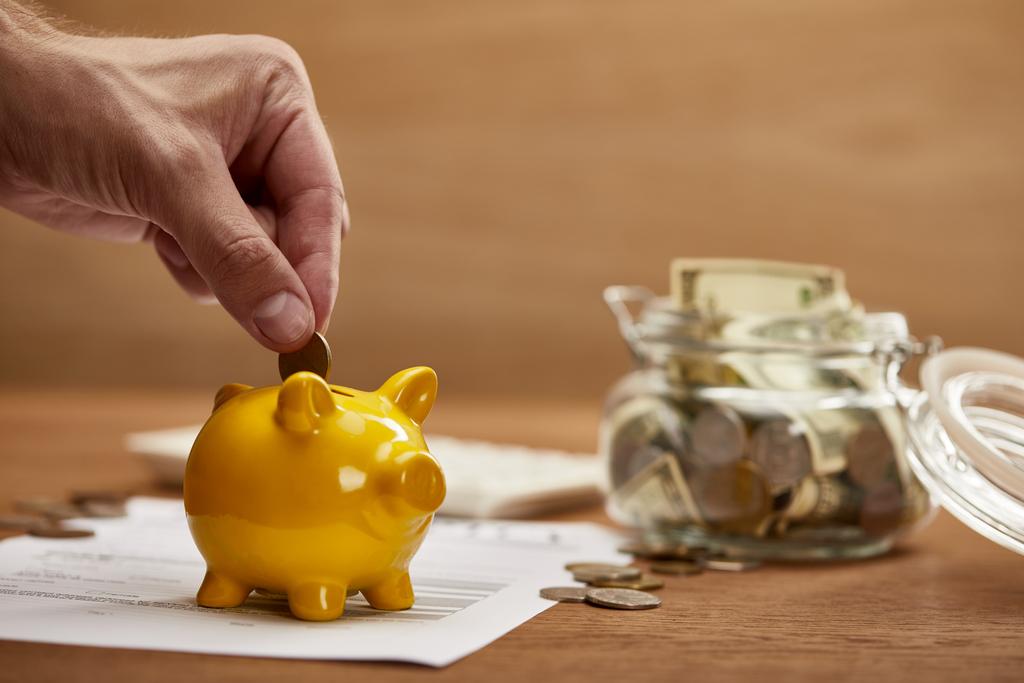 bijgesneden weergave van de man putting Coin in gele Piggy Bank - Foto, afbeelding