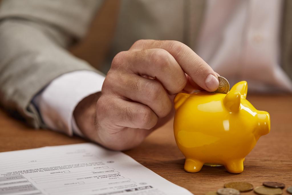 Close-up weergave van zakenman putting Coin in gele Piggy Bank op houten tafel - Foto, afbeelding