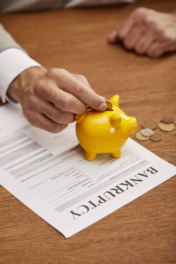 bijgesneden weergave van de man putting Coin in gele Piggy Bank op faillissement formulier - Foto, afbeelding