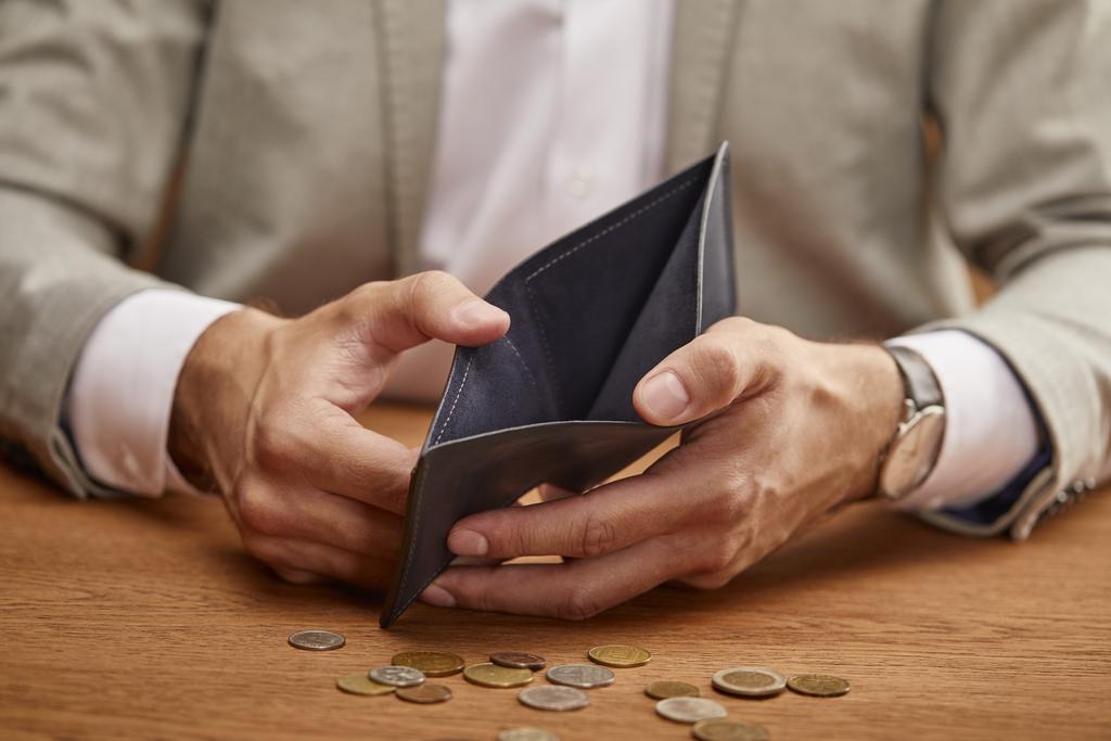 částečný pohled na člověka zobrazující prázdnou peněženku v blízkosti mincí na dřevěném stole - Fotografie, Obrázek