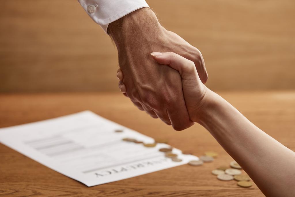 selective focus of man and woman shaking hands near bankruptcy form and coins - Photo, Image