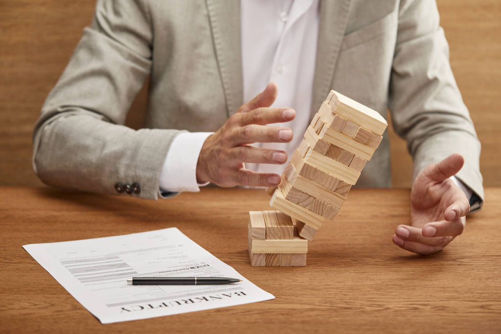 partial view of businessman in suit breaking tower made of wooden blocks near bankruptcy form - Photo, Image