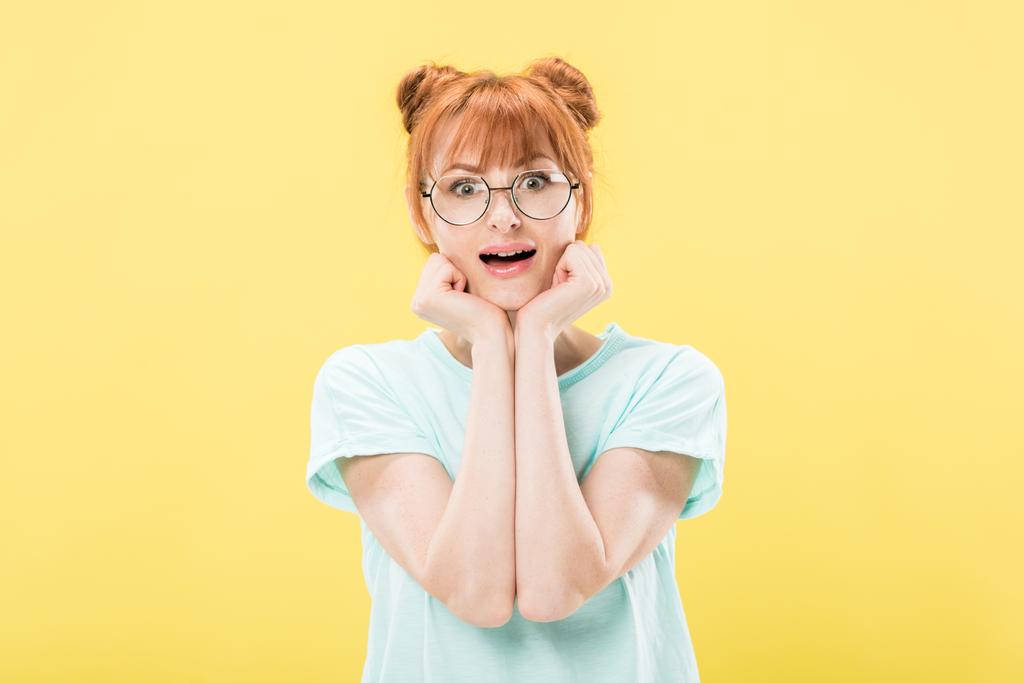 gözlük lüzmitli kızıl saçlı kızın ön görünümü elleri ile yüz propping ve sarı izole kamera bakarak - Fotoğraf, Görsel