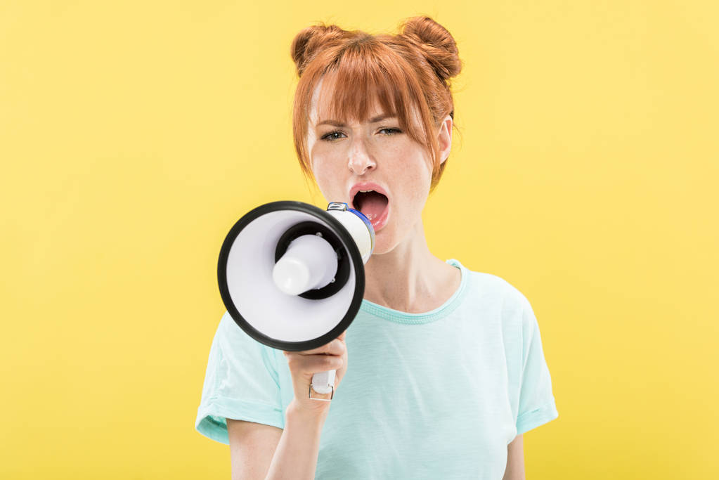 angry redhead young woman holding megaphone and screaming isolated on yellow - Photo, Image