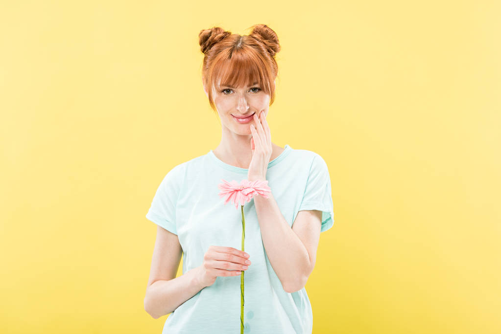 vista frontale di sorridente rossa giovane donna in t-shirt che tiene il fiore e guarda la fotocamera isolata sul giallo
 - Foto, immagini