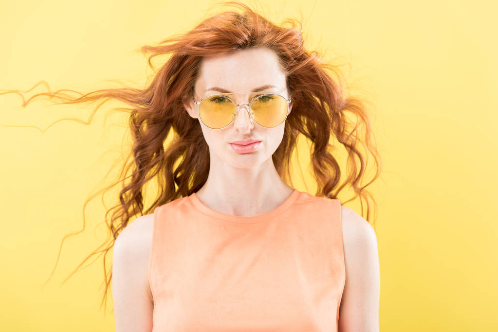 front view of serious curly redhead woman in sunglasses isolated on yellow - Photo, Image