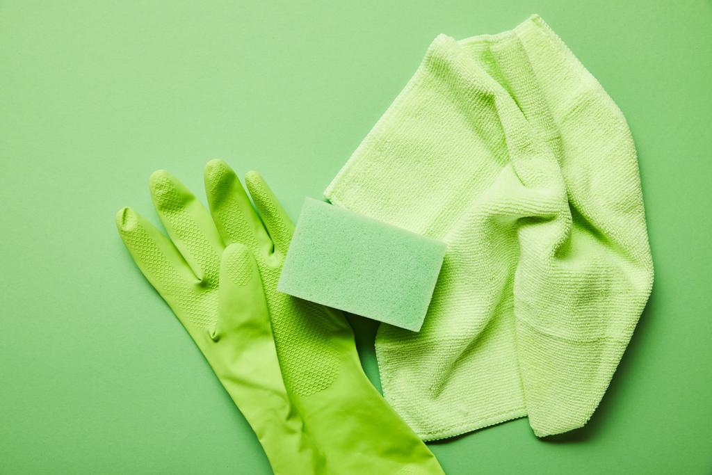 top view of colorful rag, rubber glove and sponge on green background  - Photo, Image