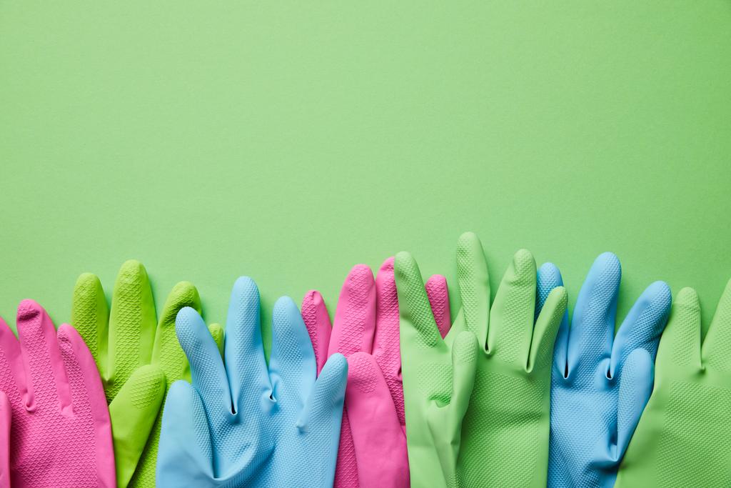 bovenaanzicht van kleurrijke en heldere rubberen handschoenen op groene achtergrond  - Foto, afbeelding