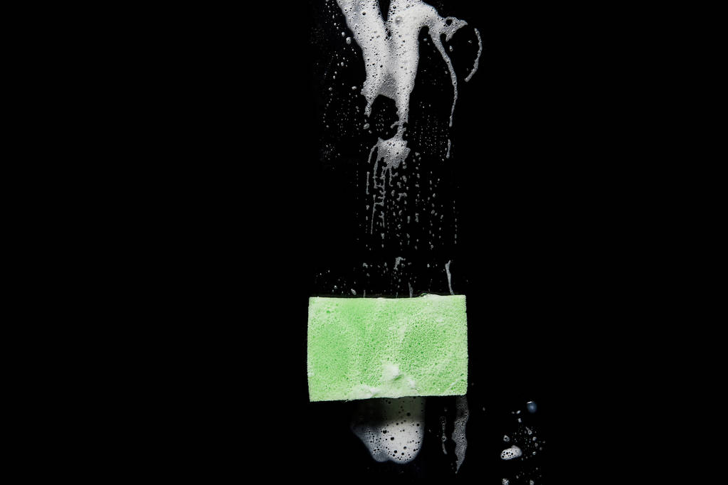 Draufsicht auf grünen und bunten Schwamm mit Schaumstoff auf schwarzem Hintergrund  - Foto, Bild