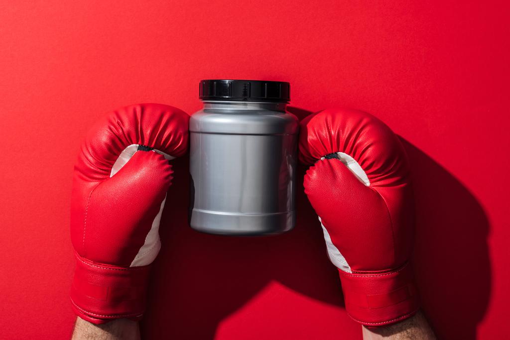 περικομμένη όψη του μπόξερ κρατώντας γκρι βάζο σε γάντια του μποξ στο κόκκινο   - Φωτογραφία, εικόνα