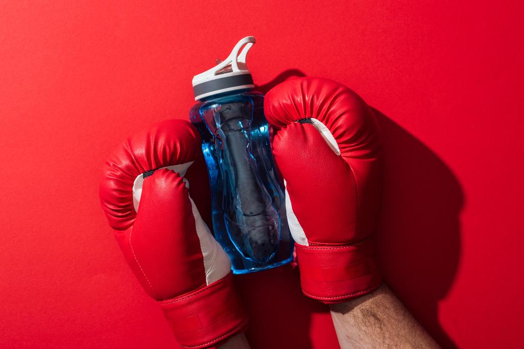 vue recadrée du boxeur tenant une bouteille de sport avec des gants de boxe sur rouge
  - Photo, image