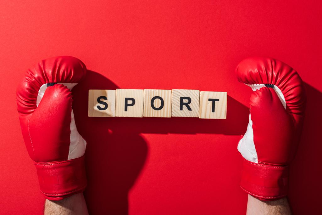 обрізаний вид людини в боксерських рукавичках біля дерев'яних кубиків зі спортивним написом на червоному
  - Фото, зображення