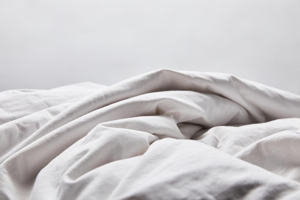 τσαλακωμένη άσπρη κουβέρτα στο κρεβάτι απομονωμένη σε γκρι - Φωτογραφία, εικόνα
