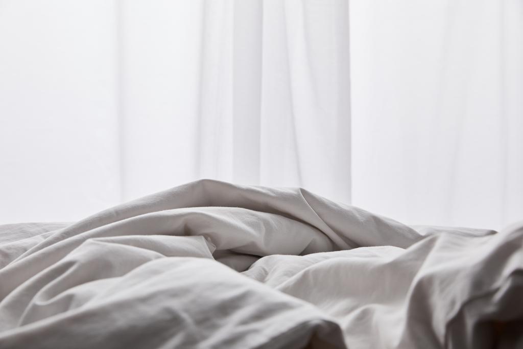 gyűrött fehér pamut takaró ágyban a függöny közelében - Fotó, kép