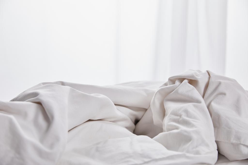 verfrommeld witte deken in bed in de buurt van gordijn - Foto, afbeelding