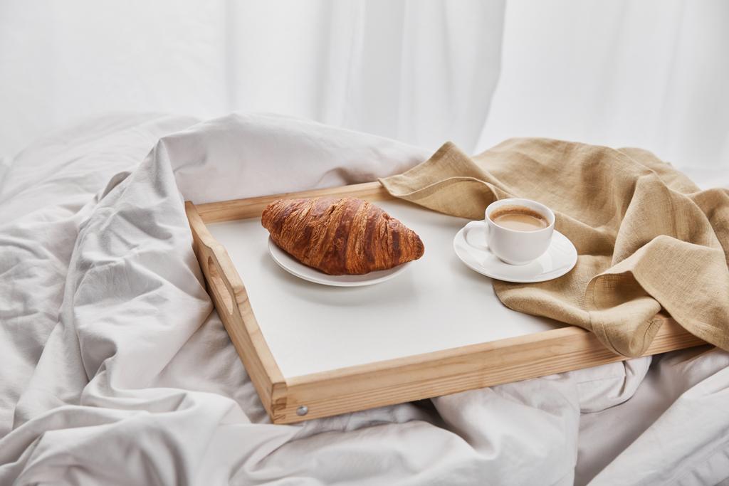 fresh croissant with coffee and napkin on wooden tray in bed at morning - Photo, Image