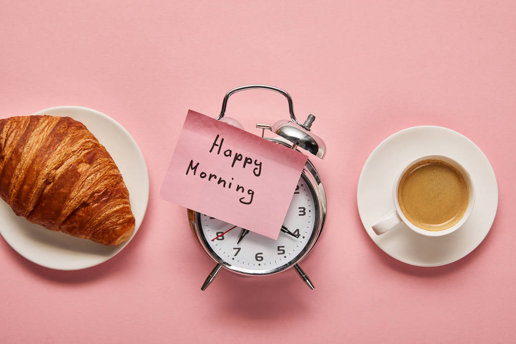 top view of alarm clock with happy morning lettering on sticky note near coffee and croissant on pink background - Photo, Image