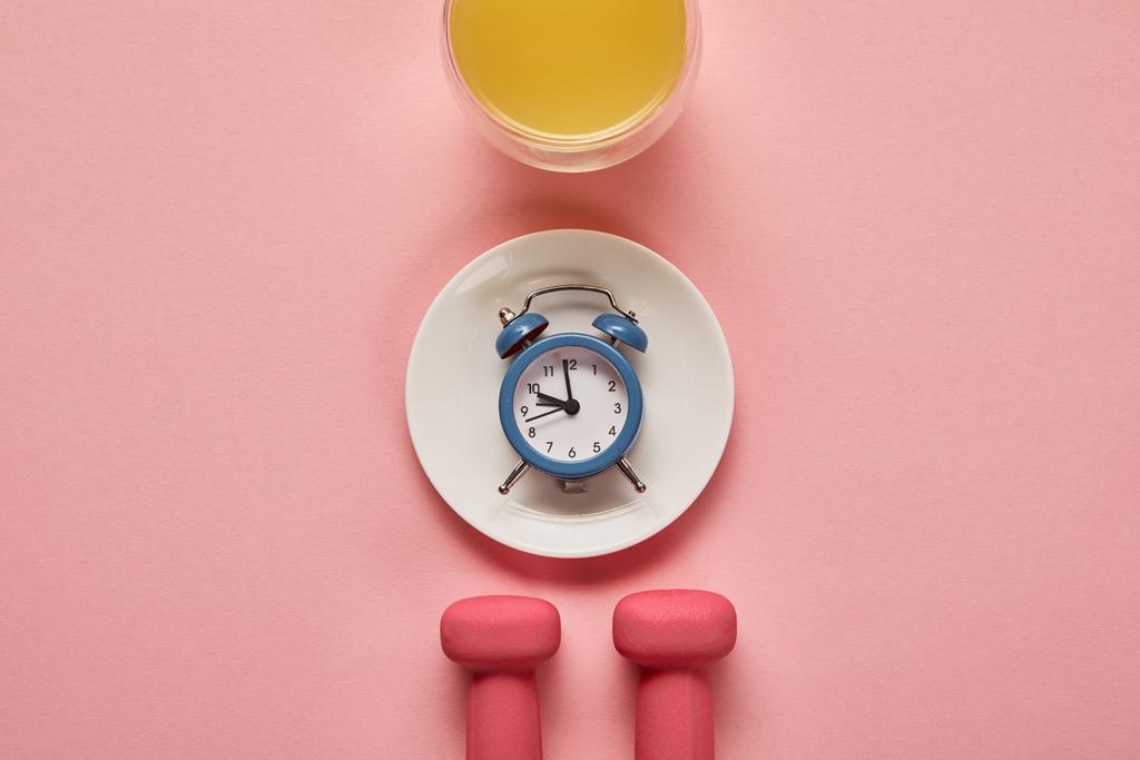 top view of dumbbells and plate with toy alarm clock near glass with orange juice on pink background - Photo, Image