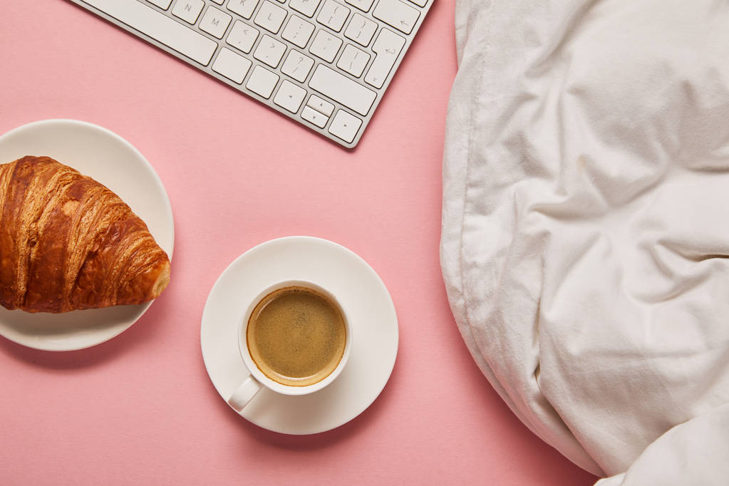 vista superior de cobertor, teclado do computador, café e croissant no fundo rosa
 - Foto, Imagem