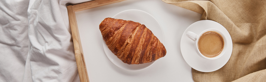 vista superior de croissant fresco con café en bandeja de madera en la cama por la mañana, plano panorámico
 - Foto, Imagen