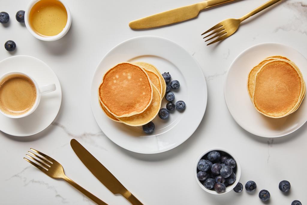 top view of pancakes, cup of coffee and scattered blueberries near golden cutlery - Photo, Image