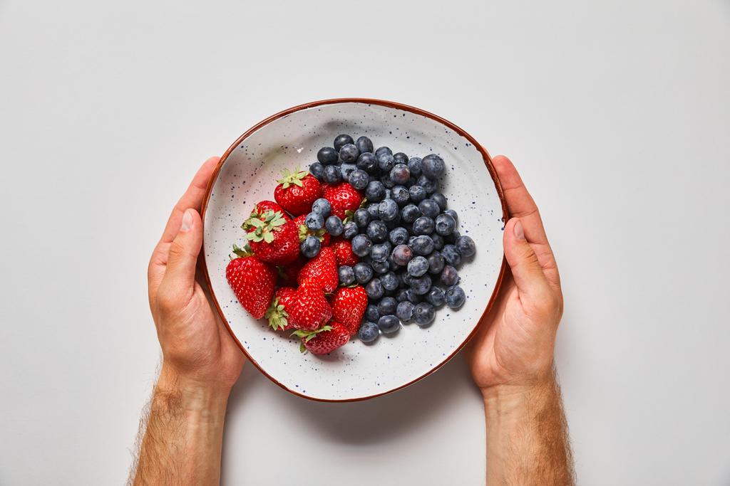 vue recadrée de l'homme tenant grande assiette avec de savoureuses fraises et des baies bleues
 - Photo, image